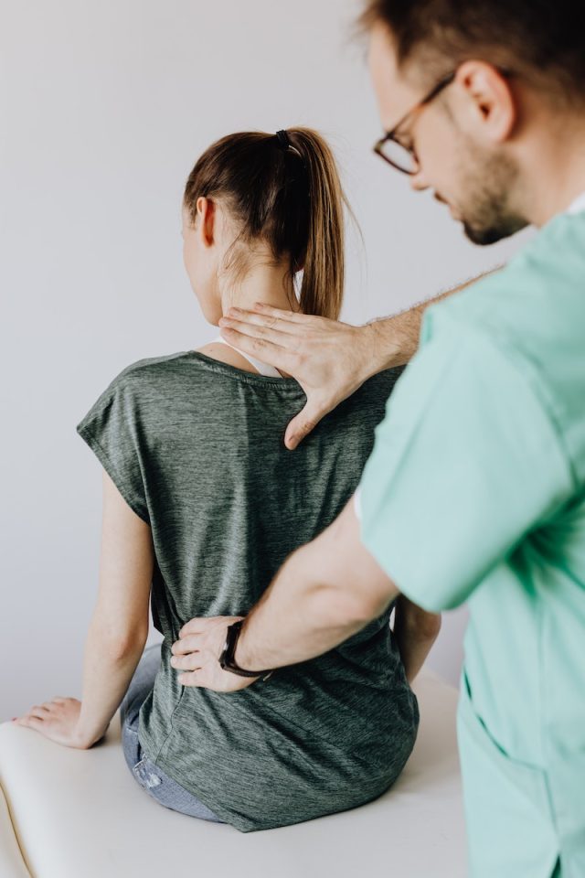 Crop osteopath checking up back of anonymous patient in hospital