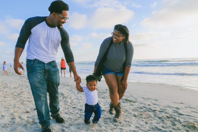 man in black and white striped long sleeve shirt holding baby in white shirt on beach